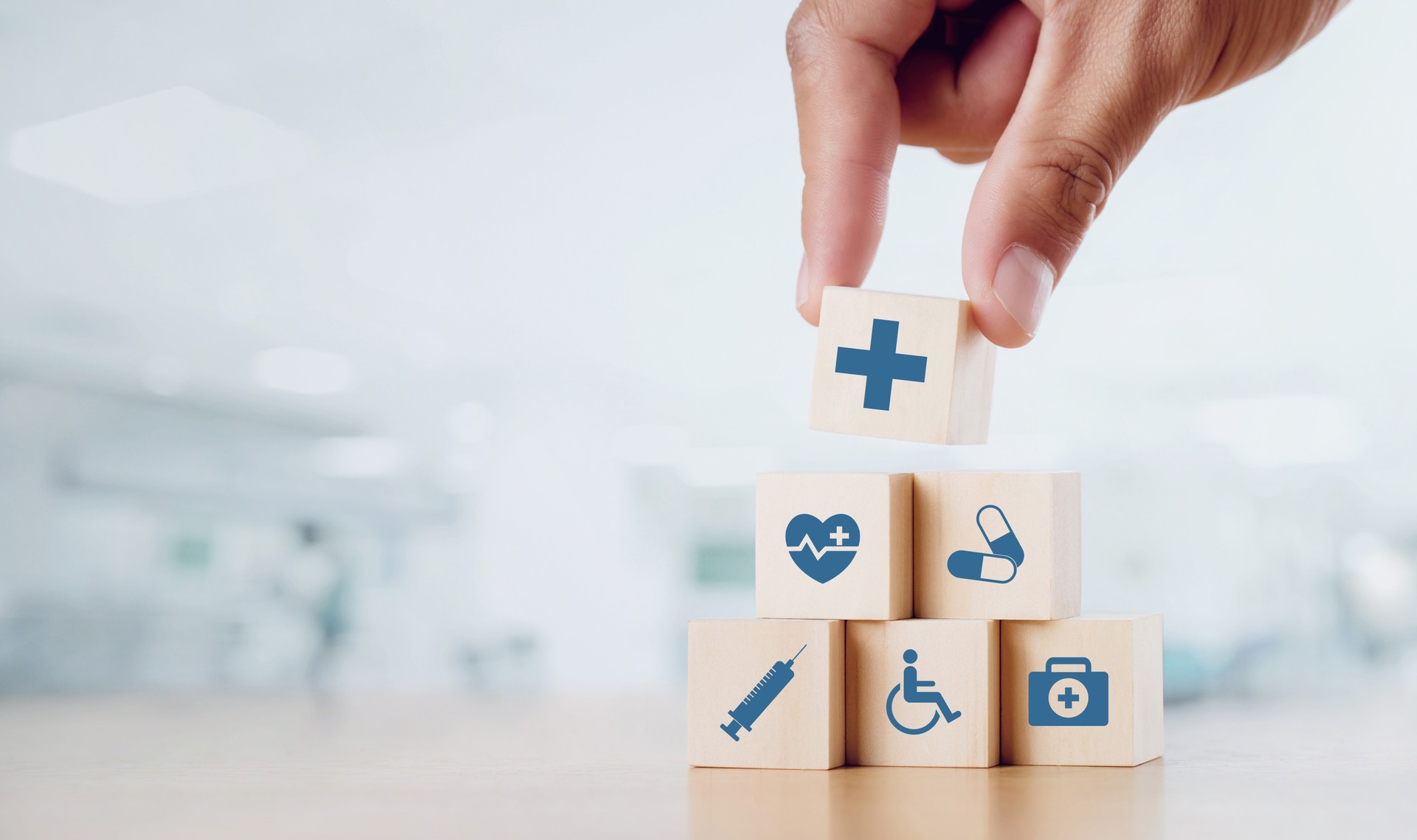 Close up man hand arranging wood block with healthcare medical icon on hospital background. Health care and Health insurance concept.