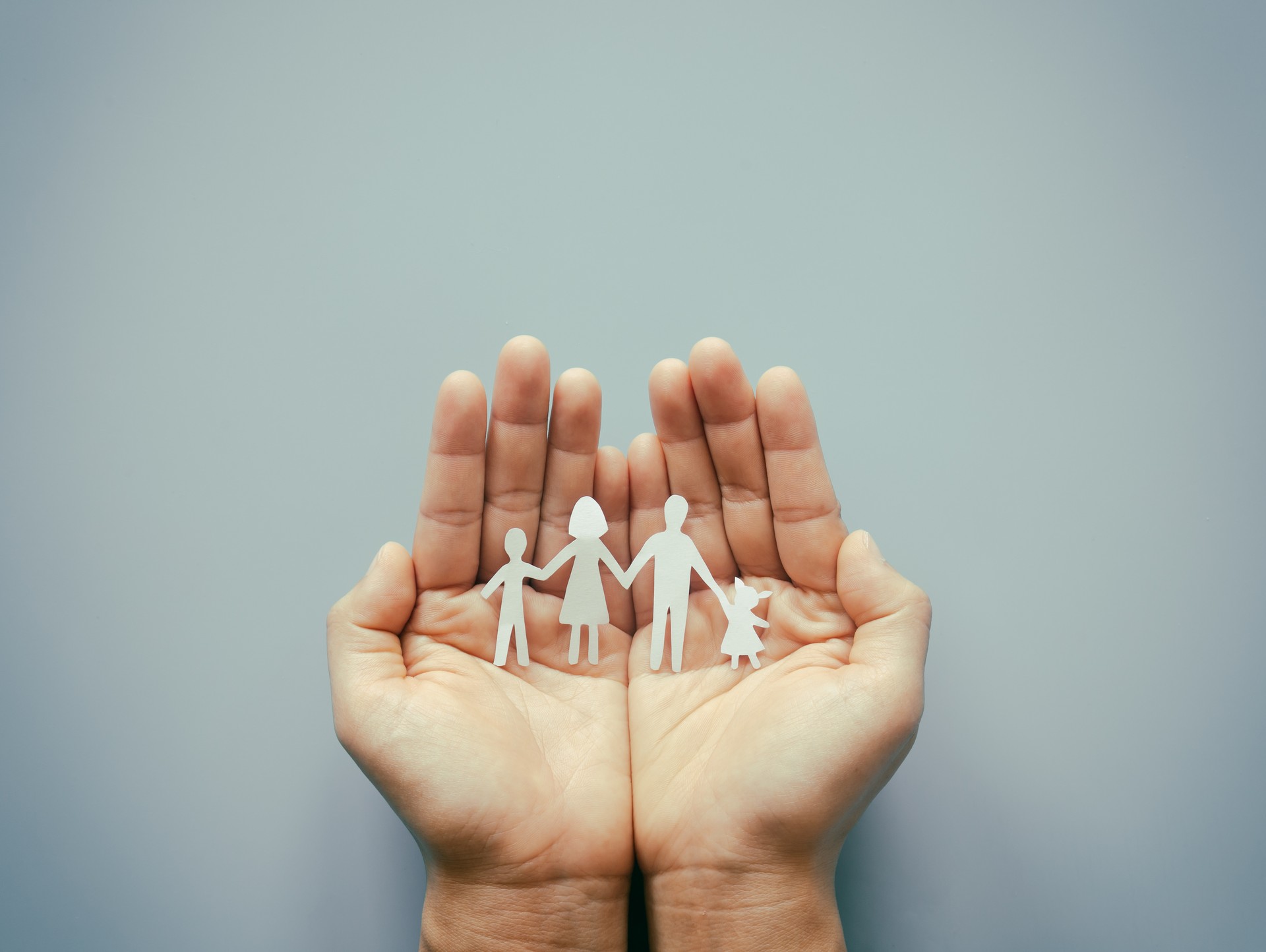 Hand holding family paper cut on blue background. Family day concept, foster care, domestic violence, homeschool, international day of families, world mental health day, world autism awareness day.