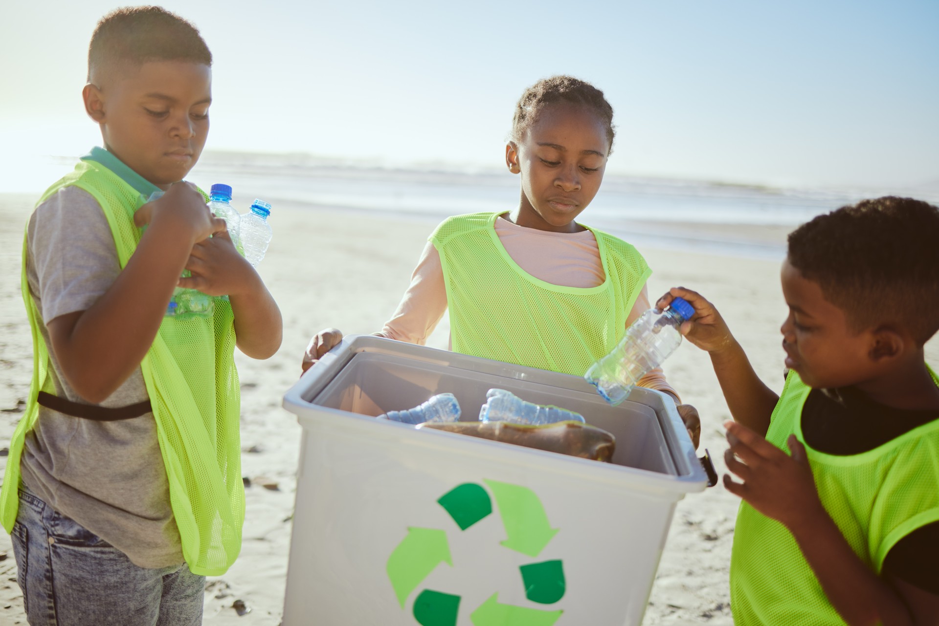 Group of children cleaning beach or recycling plastic for education, learning or community help in climate change project, ngo and charity. African friends with recycle box and teamwork on earth day